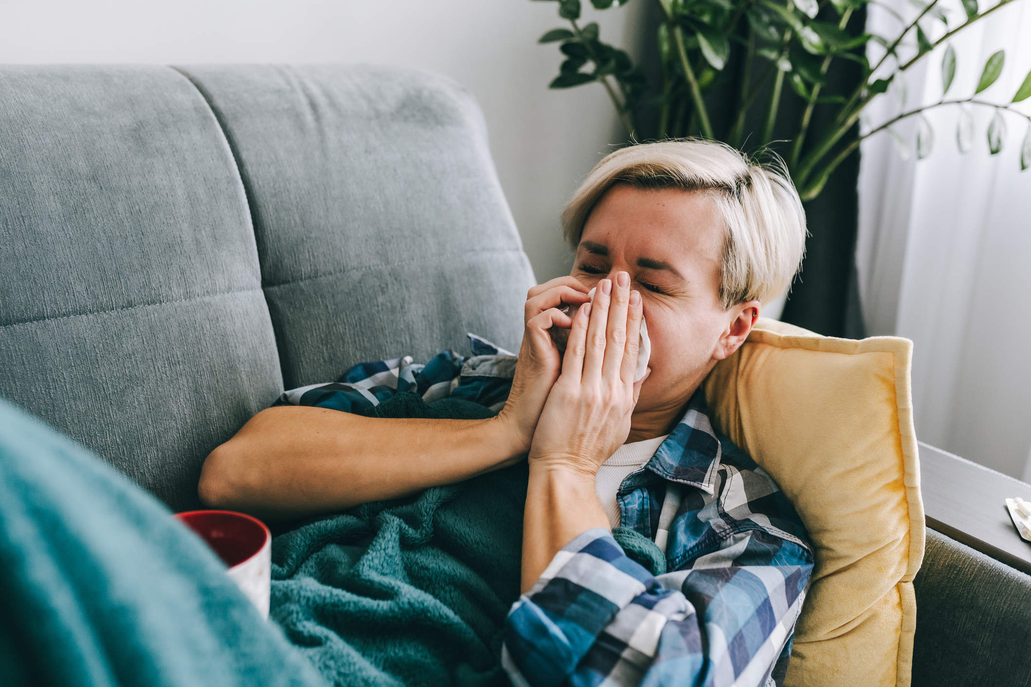 A woman lying on the sofa blowing her nose