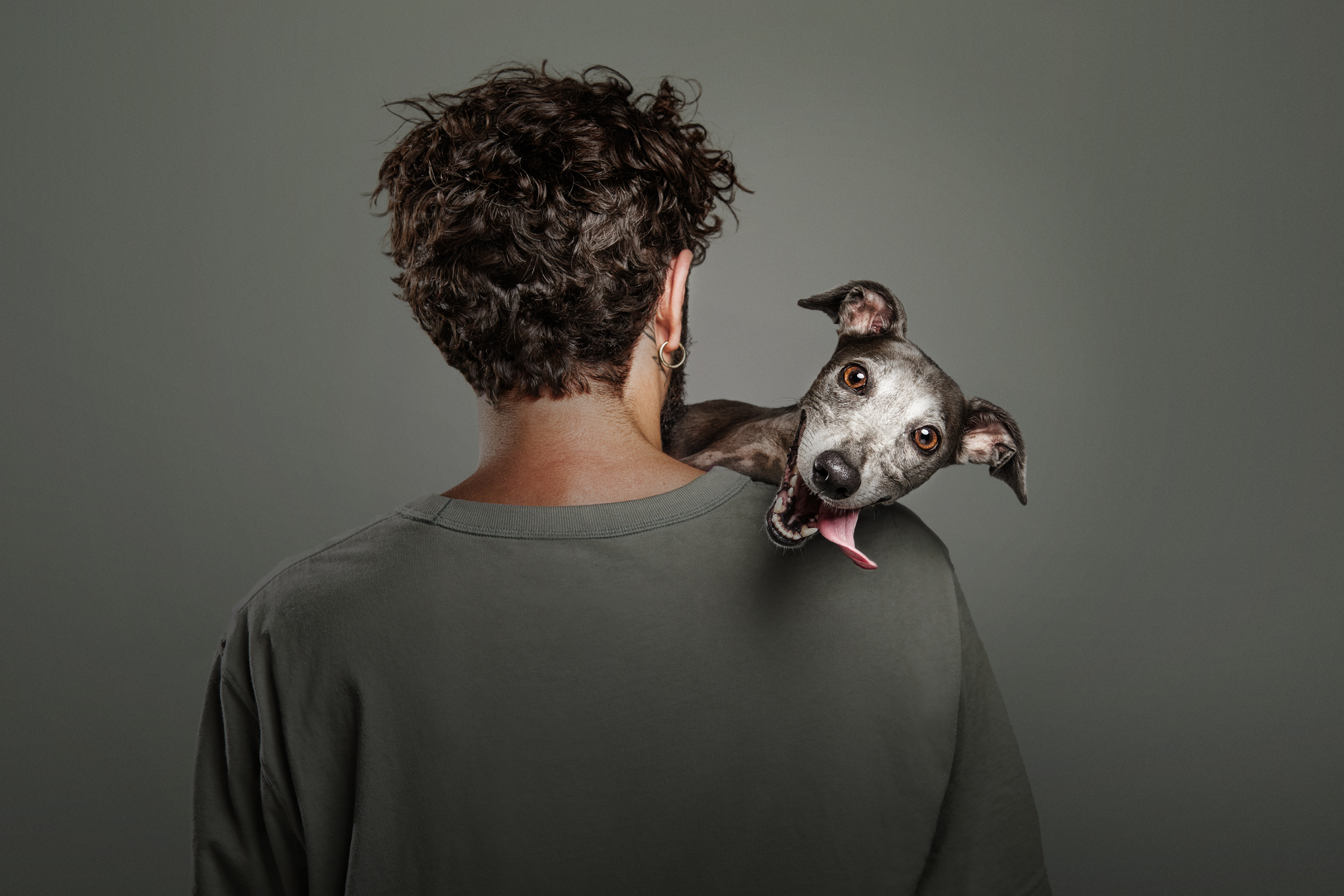 A dog leaning over its owners shoulder looking at the camera