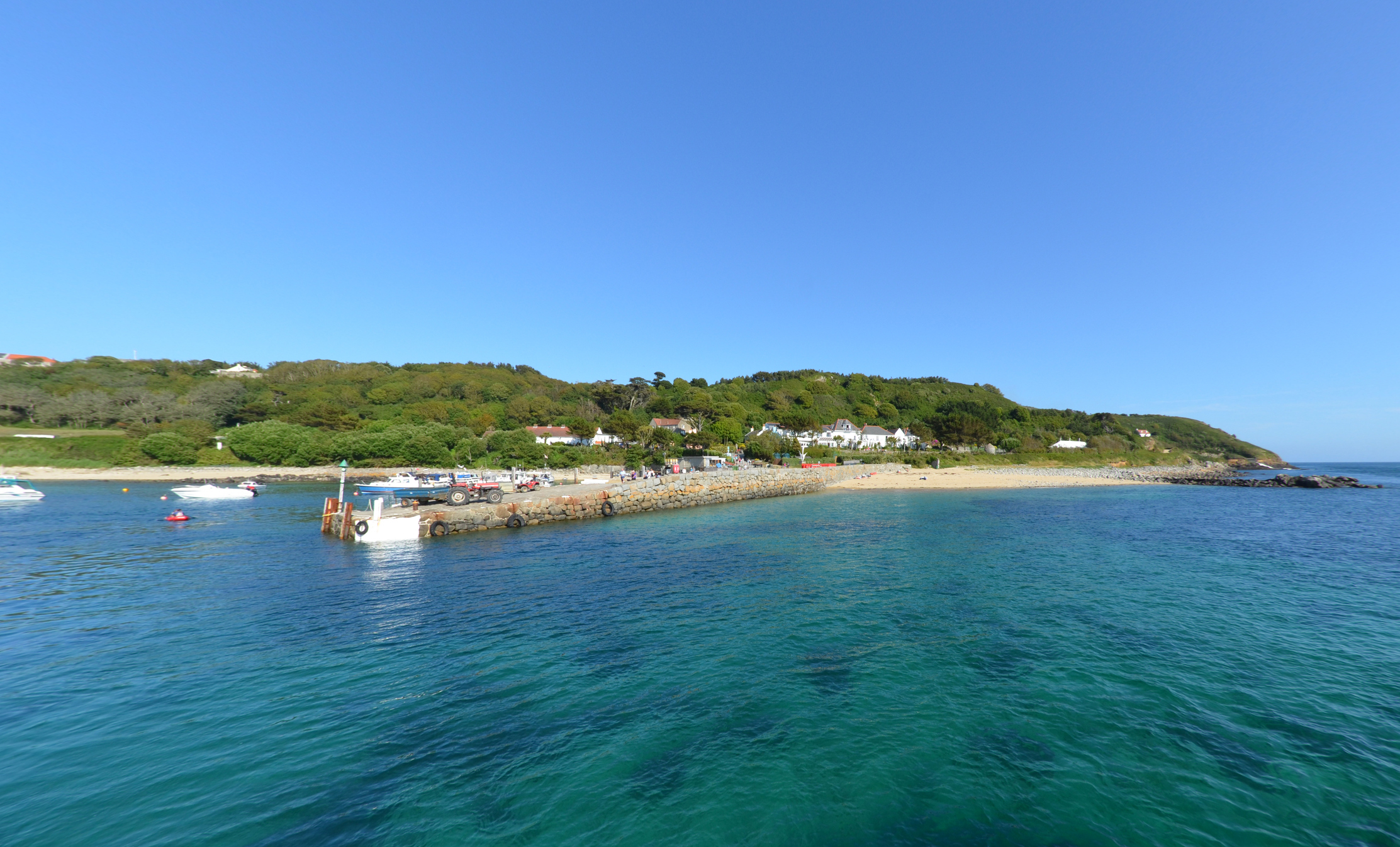 Approaching Herm Island quay from the water, part of the Channel Islands. Other boats and people in the distance (too small to be recognisable).