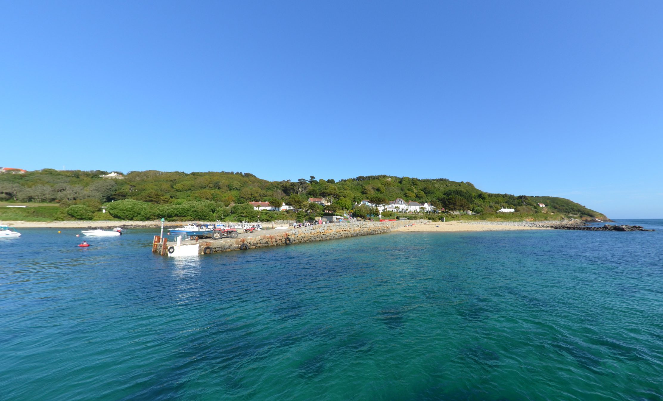 Approaching Herm Island quay from the water, part of the Channel Islands. Other boats and people in the distance (too small to be recognisable).