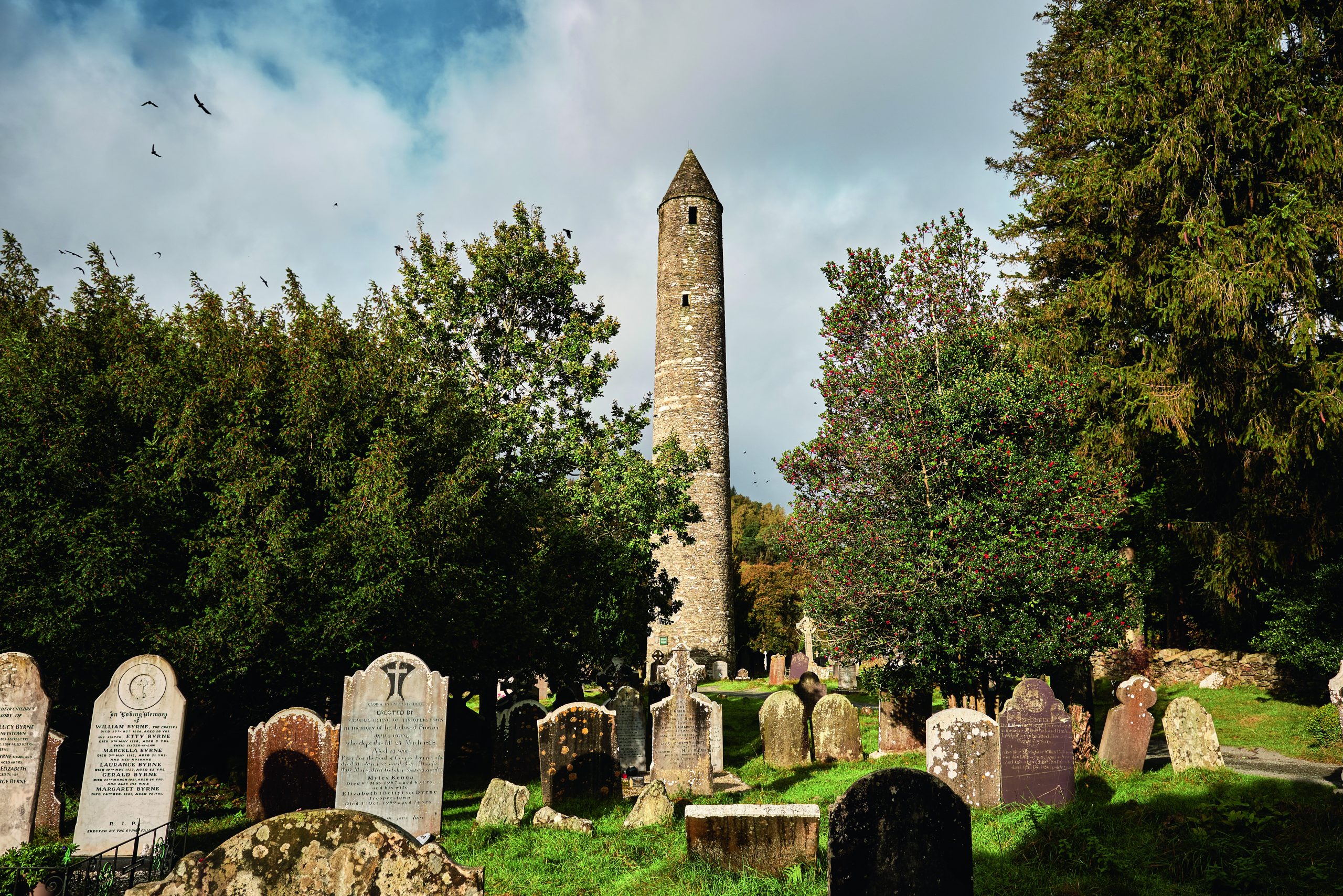 Glendalough, Ireland; 17th of October 2024. A scenic view of the iconic round tower and ancient gravestones at Glendalough, Ireland, surrounded by trees and nature, capturing Irish medieval heritage and spiritual atmosphere.