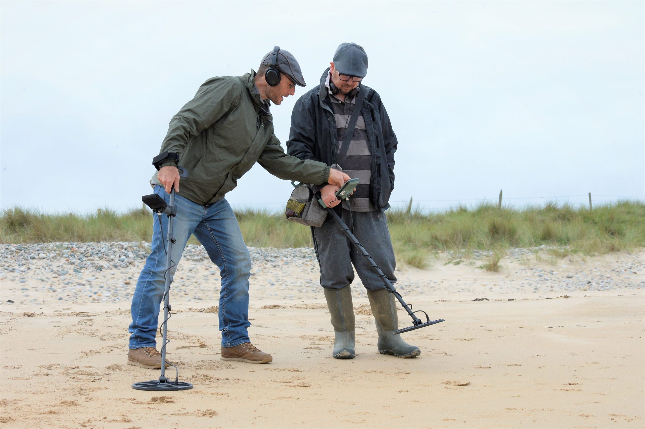 Two men using their metal detector at the beach.