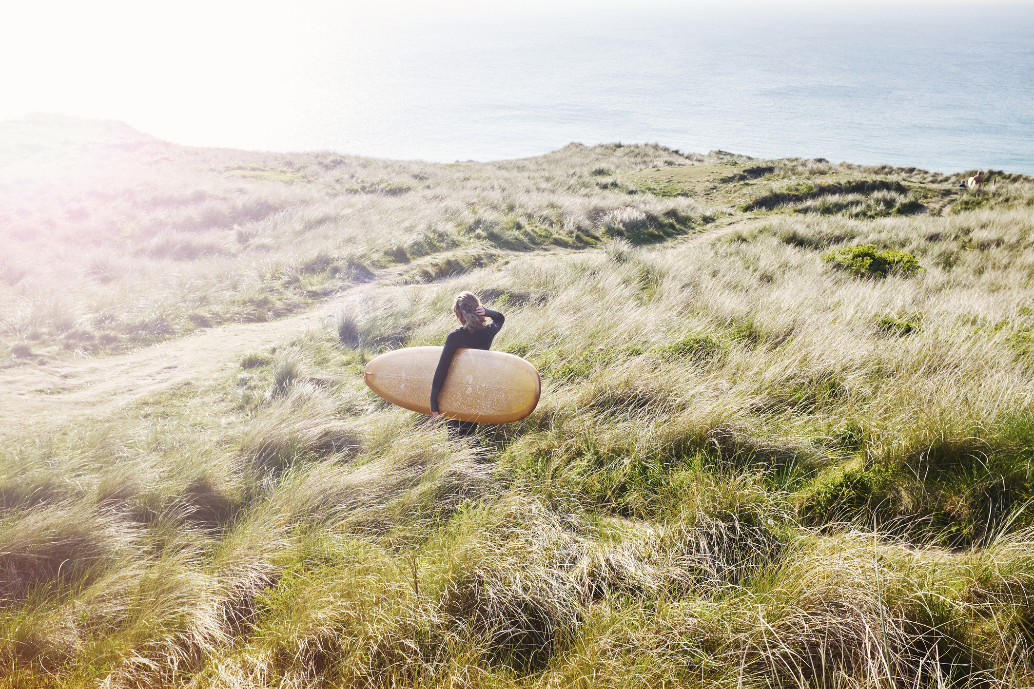 A surfer walking over the hill to the beach