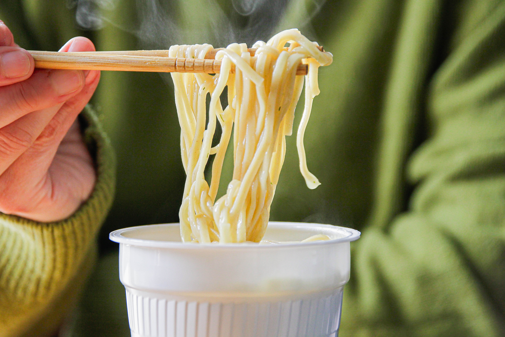 A person picking up noodles from a pot using chopsticks
