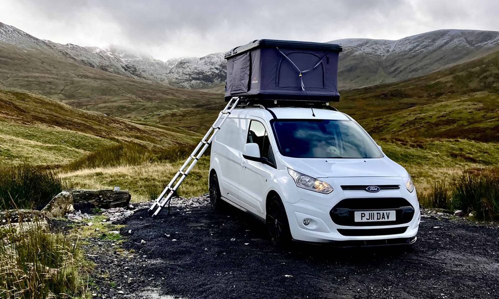 White van parked on sweeping moorland with a black tent box on the roof