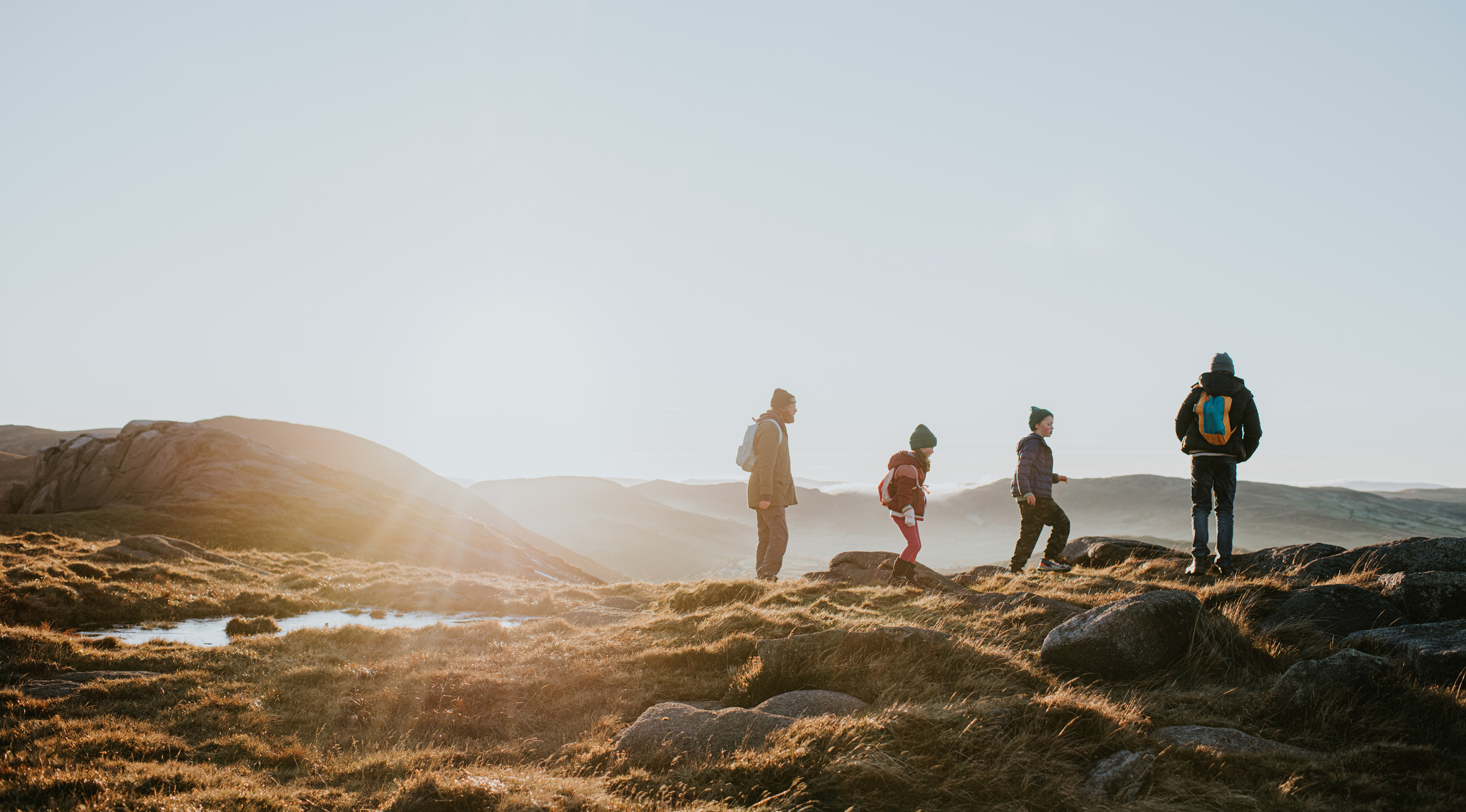 A family walking over a hilltop with the sun setting in the background