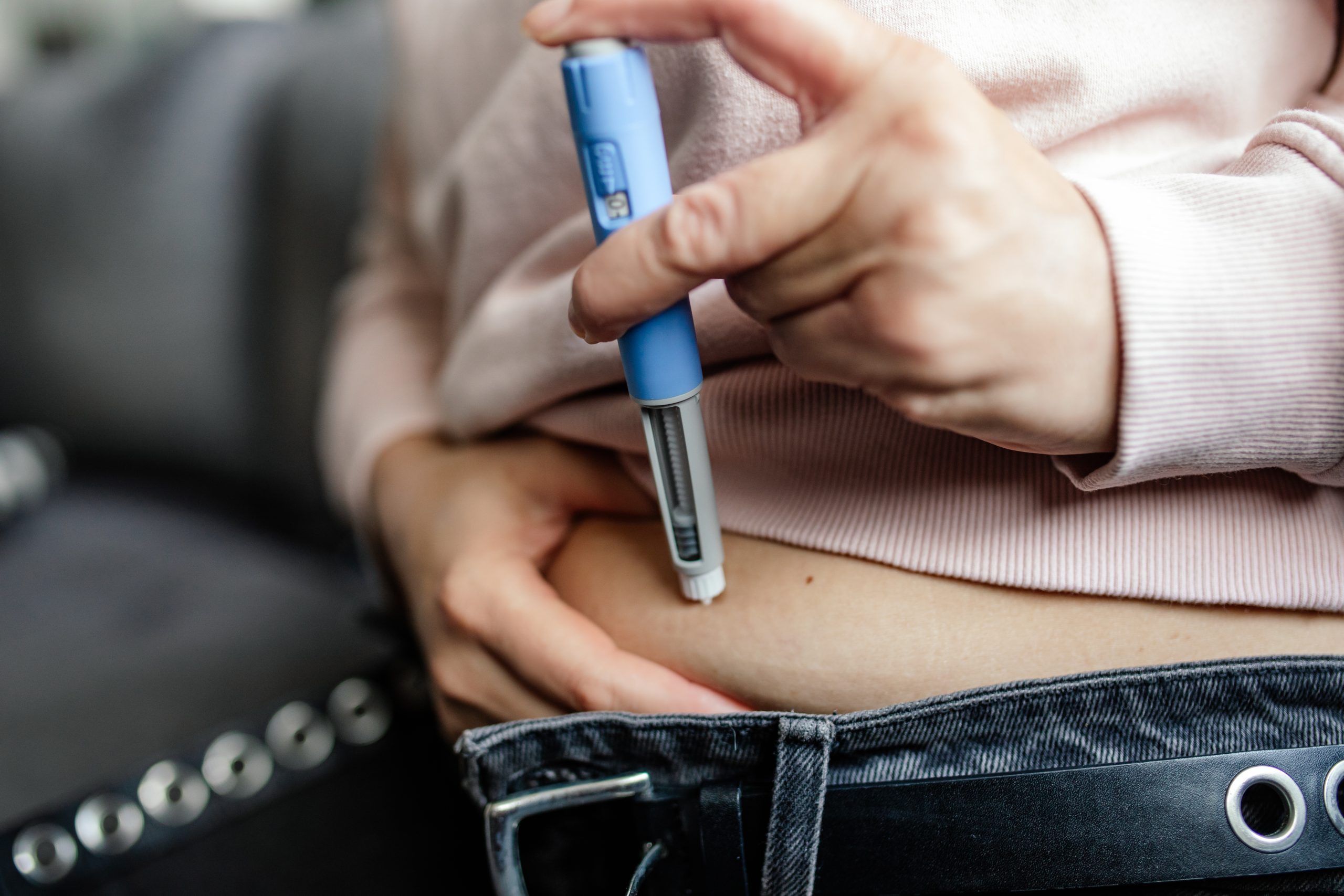 A woman performs a subcutaneous self-injection with a semaglutide pen into her abdomen. This modern weight loss and diabetes treatment highlights a personal healthcare routine at home.