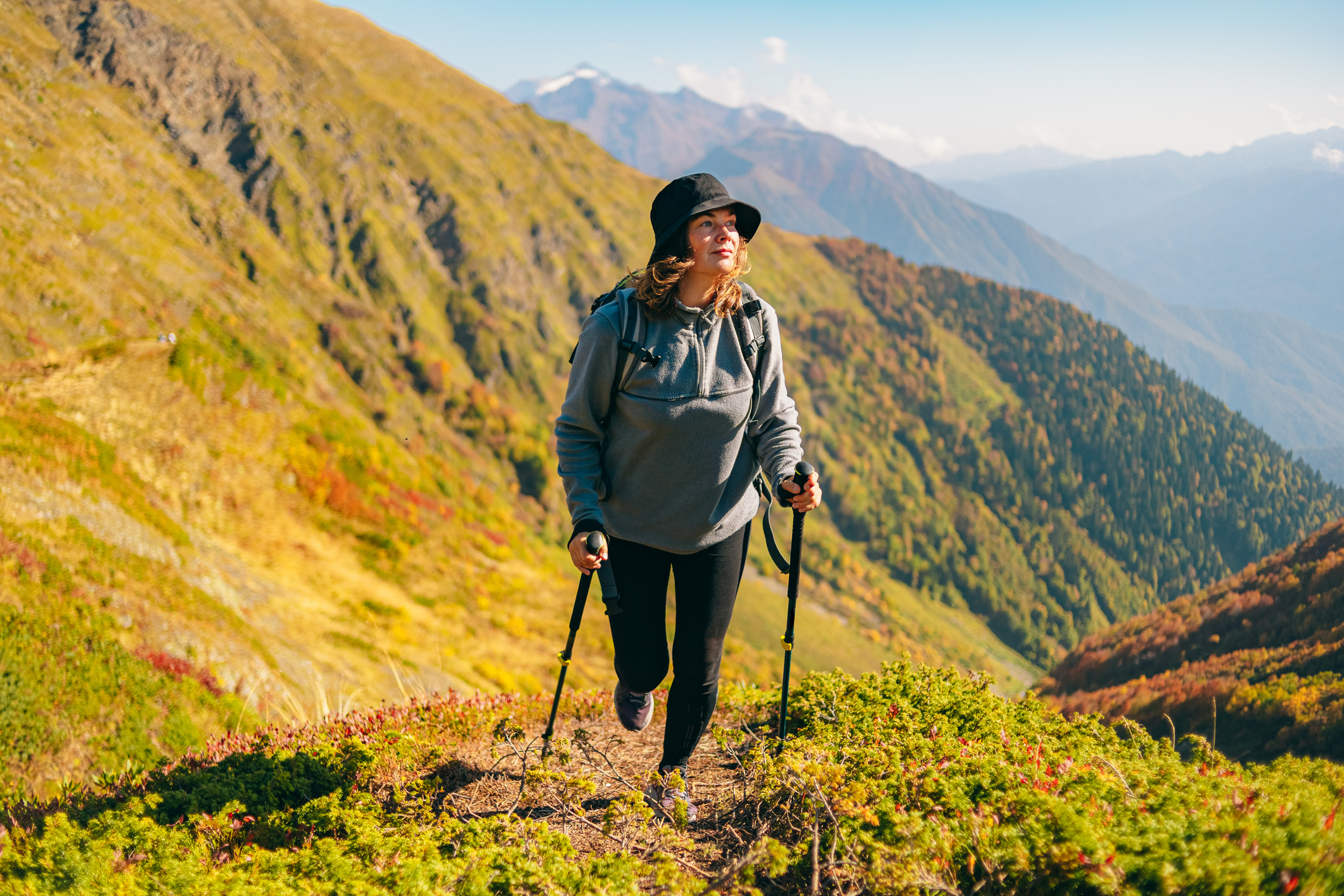 A woman walks up a hill using walking poles