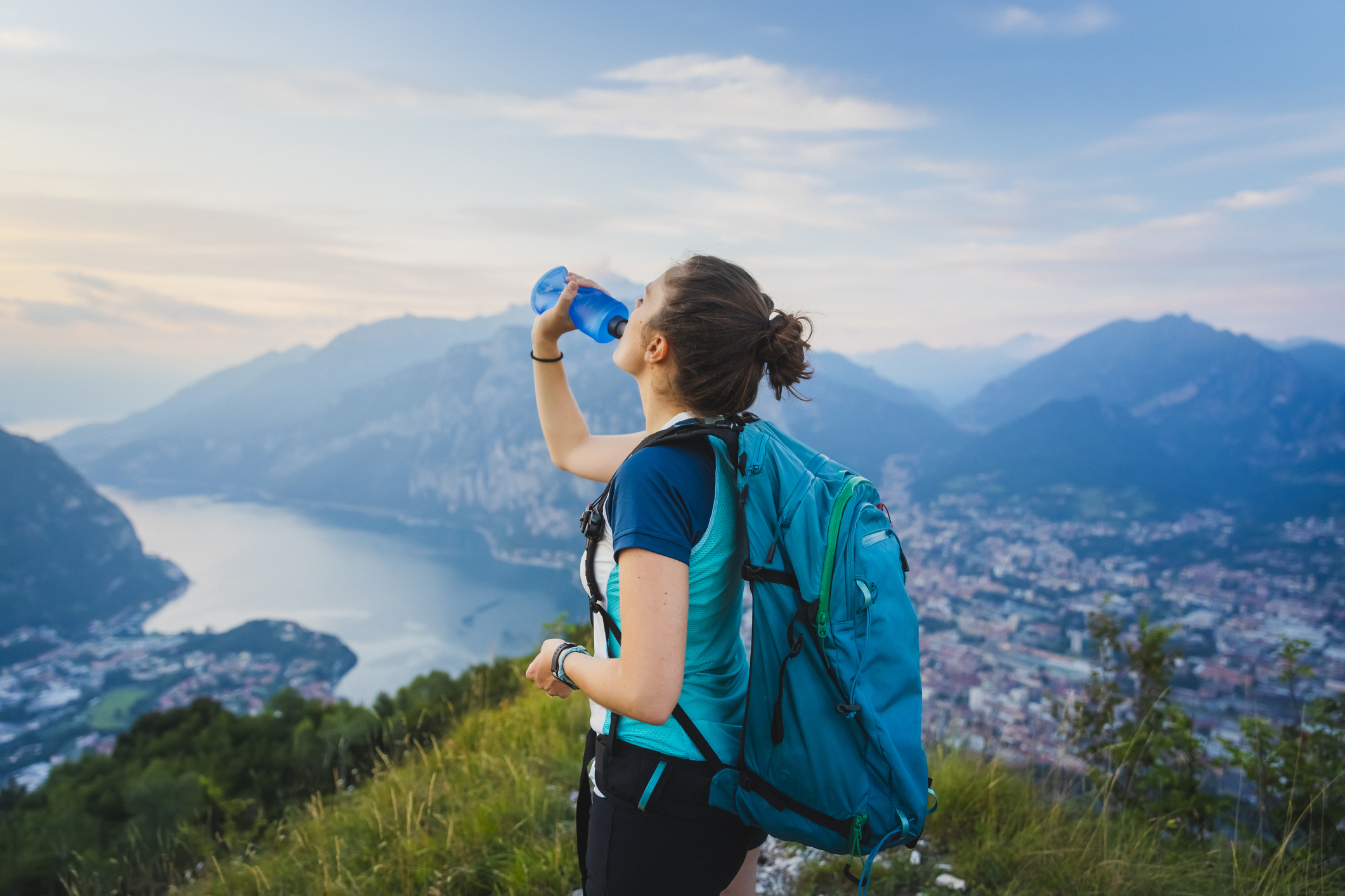 A woman drinks water out of a bottle at the top of a hike up a big hill