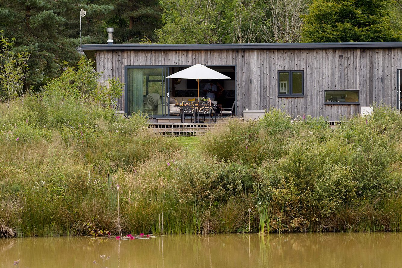 Single-storey wooden building with large glass front and deck overlooking a river