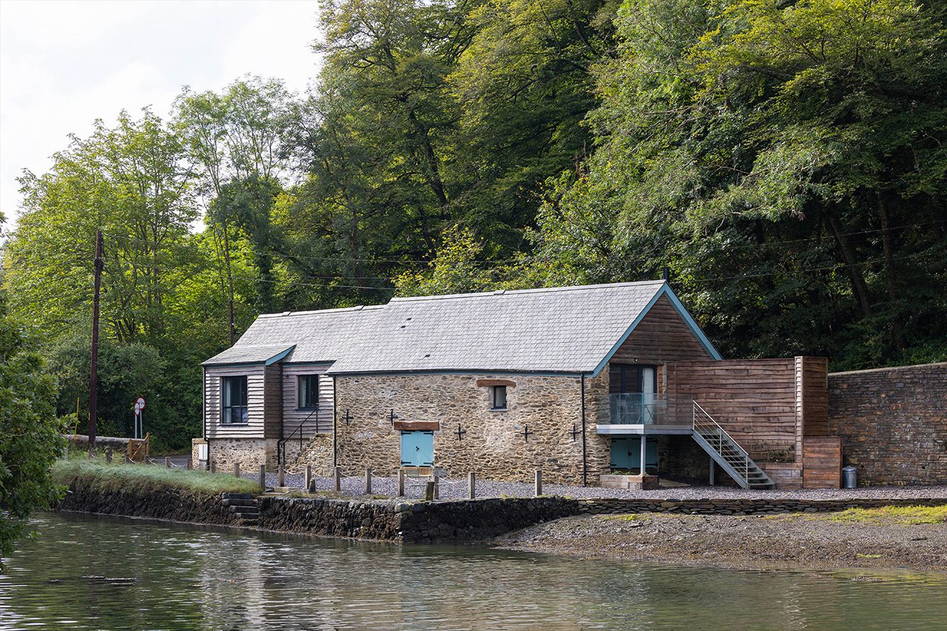 Low stone building on the river edge surrounded by trees and a decking area
