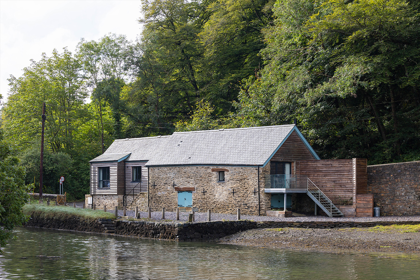 Low stone building on the river edge surrounded by trees and a decking area