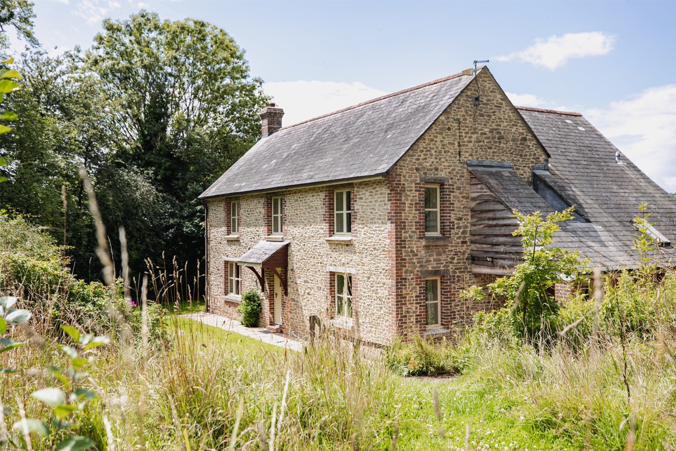 Large brown stone cottage surrounded by meadow grass
