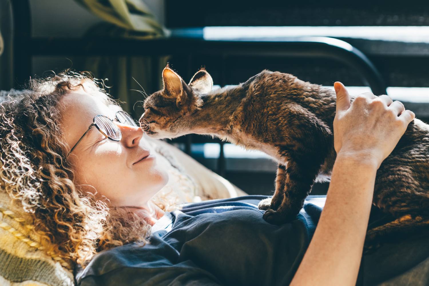A woman lying on the floor playing with her cat on top of her.