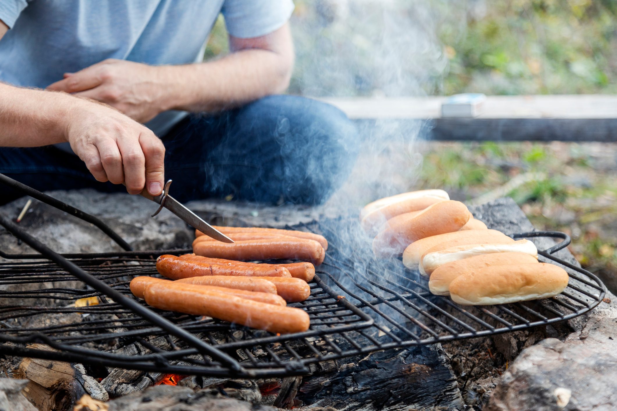 Midsection of man grilling sausages and buns on grill