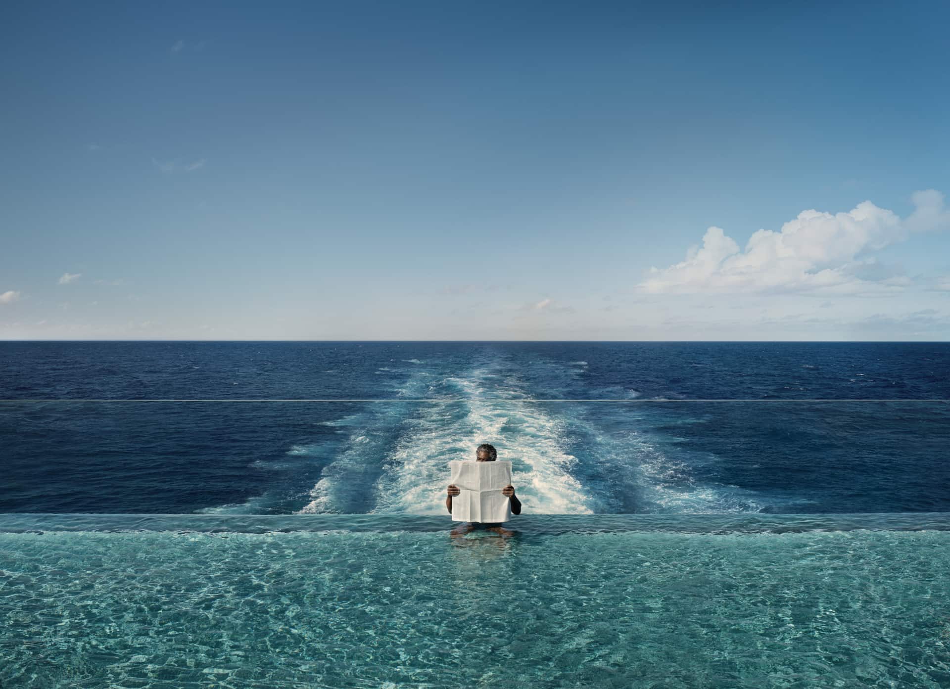 Woman reading a newspaper in an infinity pool on a ship with the sea stretching out behind