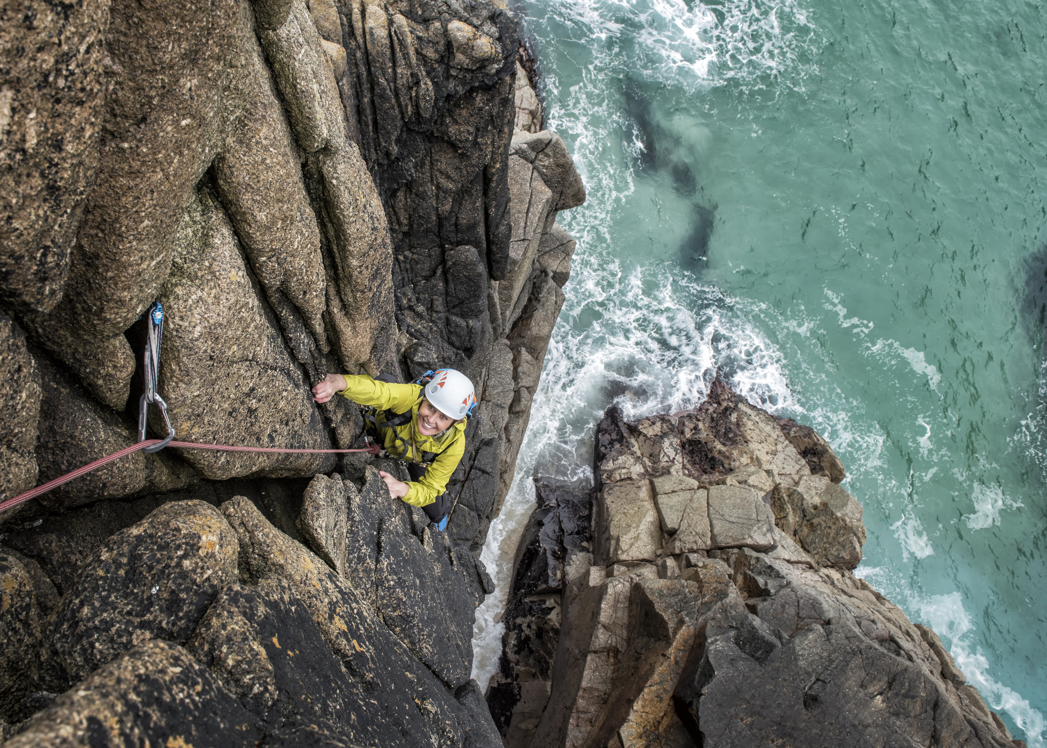 A woman climbs up a cliff face in Cornwall with the sea below her