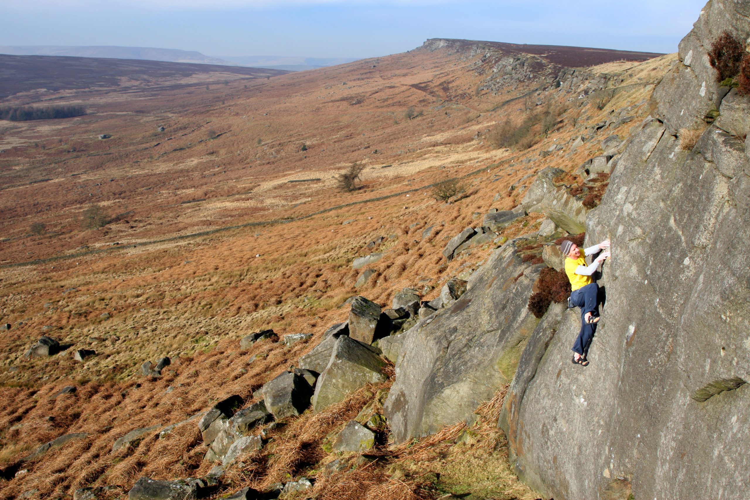A woman climbing up a cliff face in the Peak District